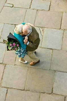 an older man is walking down the street with flowers in his hand and holding a bouquet