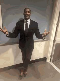 a man wearing a suit and tie standing in front of a door with his hands out