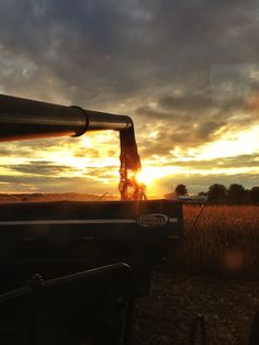 the sun is setting over a farm field with a tractor in the foreground and an old grain silo in the background