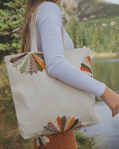 a woman carrying a white tote bag by a lake