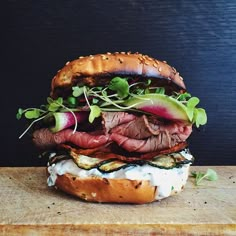 a large sandwich with meat, lettuce and onions on it sitting on a wooden table