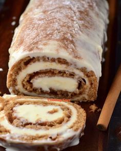 a cinnamon roll is cut in half and sitting on a cutting board next to two cinnamon sticks