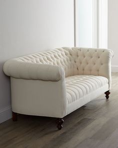 a white couch sitting on top of a hard wood floor next to a wall and window