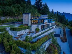 an aerial view of a modern home in the mountains at dusk with trees and shrubs surrounding it