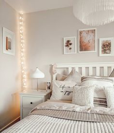 a white bed topped with lots of pillows next to a night stand and lights on the wall