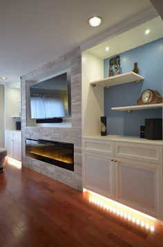 a living room with wood floors and a fireplace in the center is lit by recessed lights