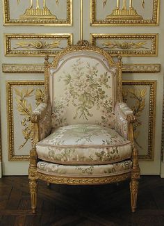 an ornately decorated chair sits in front of gold painted doors and wood flooring