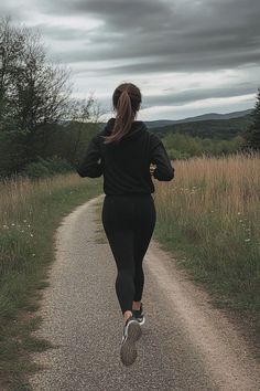 a woman running down a dirt road next to tall grass