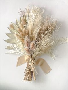 a bouquet of dried flowers and leaves on a white surface with a ribbon tied around it