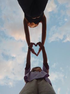 two people making a heart shape with their hands in the air, against a cloudy blue sky