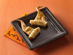 two pieces of fried food on a black plate next to an orange and black napkin