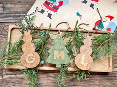 three wooden ornaments are hanging from a tray on a table with pine branches and other decorations