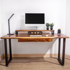 a wooden desk with a computer monitor and keyboard on it in front of a white wall