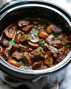 a crock pot filled with beef and mushrooms, garnished with parsley