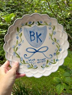 a person holding up a plate with the initials on it in front of some trees