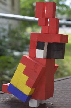 a red and yellow lego figure sitting on top of a wooden table next to trees