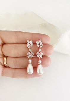 a person is holding two pairs of earrings in their hand, one with pearls and the other with leaves on it