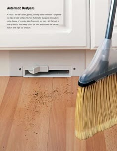 a broom is laying on the floor in front of a white cabinet with an automatic dustpan