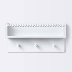 a white wall shelf with three hooks on the front and two balls on the back