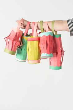 a person is holding up some colorful paper objects that are hanging in the air with their hands