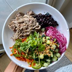 a person holding a white bowl filled with different types of vegetables and meats on top of it