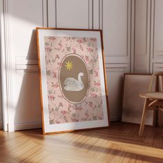 a white swan sitting on top of a wooden floor in front of a framed picture