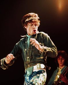 a young man is performing on stage with his hands in the air and another person behind him