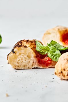 a piece of pizza with basil and tomato sauce on it next to other pieces of bread