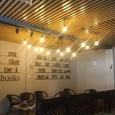 an empty restaurant with tables and chairs under the lights on the ceiling is lit by bookshelves