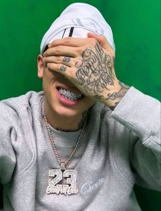 a man with tattoos covering his eyes and holding his hands up to his face while wearing a sweatshirt