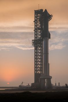 the sun is setting behind a rocket on top of a building in the distance,