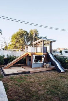 a small house with a slide in the back yard and a deck on top of it