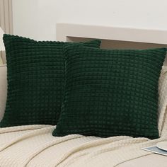 two green pillows sitting on top of a couch next to a white pillow case and a book