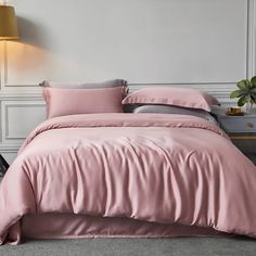 a bed with pink sheets and pillows in a room next to a lamp on a table