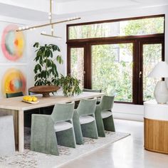 a dining room table surrounded by chairs and potted plants in front of a large window