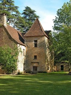 an old stone house in the middle of a green field with trees and grass around it