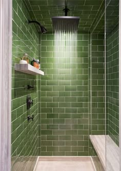 a shower with green tiles and white fixtures in it's corner, next to a shelf on the wall