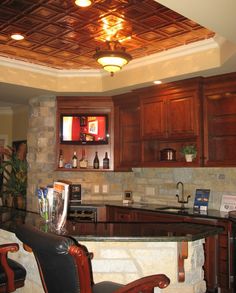 a kitchen with wooden cabinets and black leather chairs in front of a bar area that has a television on the wall