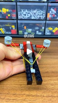 a hand is holding a lego toy on top of a wooden table with plastic bins in the background