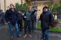 three men standing next to each other in front of a building with statues on it