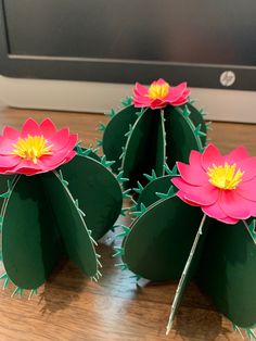 three paper flowers sitting on top of a wooden table next to a computer monitor and keyboard