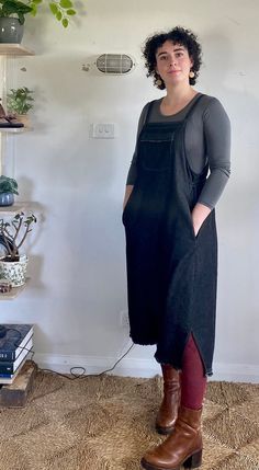 a woman standing in front of a white wall wearing boots and a black dress with red leggings