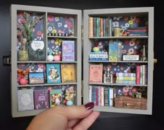 a hand holding an open book in front of a shelf filled with books