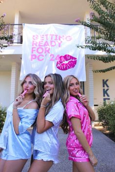 three beautiful young women standing next to each other in front of a white sign with pink lipstick on it