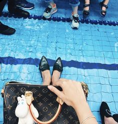 a woman's hand holding onto a purse with her feet on the ground next to other people