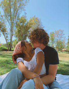 a man and woman are sitting on the grass together, one is kissing the other's cheek