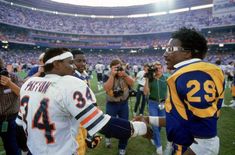 two football players shaking hands in front of an audience at a stadium with cameras around them