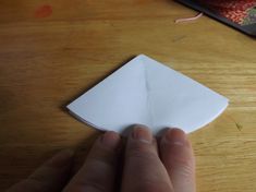 a hand holding an origami piece on top of a wooden table