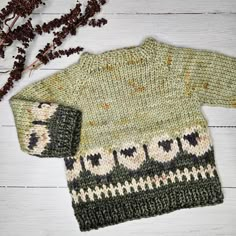 a green sweater and hat sitting on top of a white wooden floor next to dried flowers