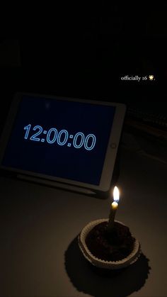 a lit candle sitting in front of a tablet with the date 12 00 on it